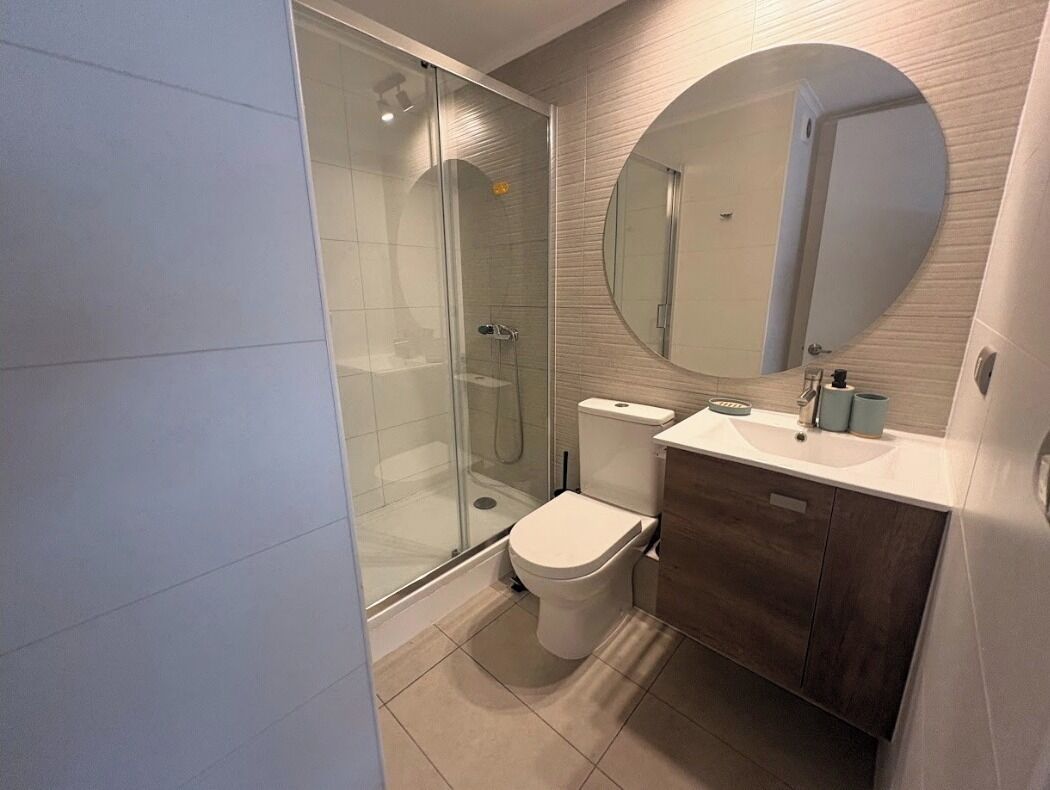 A modern bathroom with a glass shower enclosure, a toilet, a sink, and a large mirror.