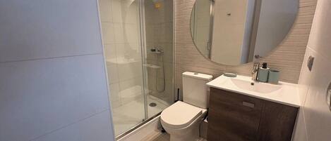 Une salle de bain moderne avec une douche à parois de verre, des toilettes, un lavabo et un grand miroir.