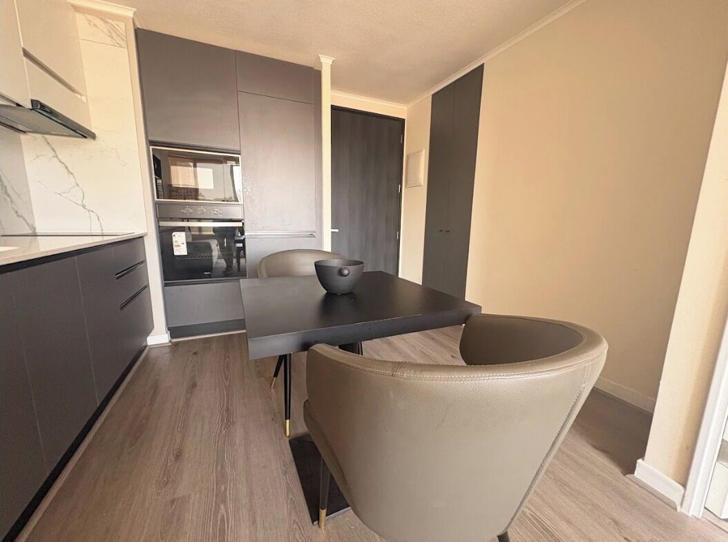 A modern kitchen with dark cabinets, a marble countertop, and a dining area with a table and chair.