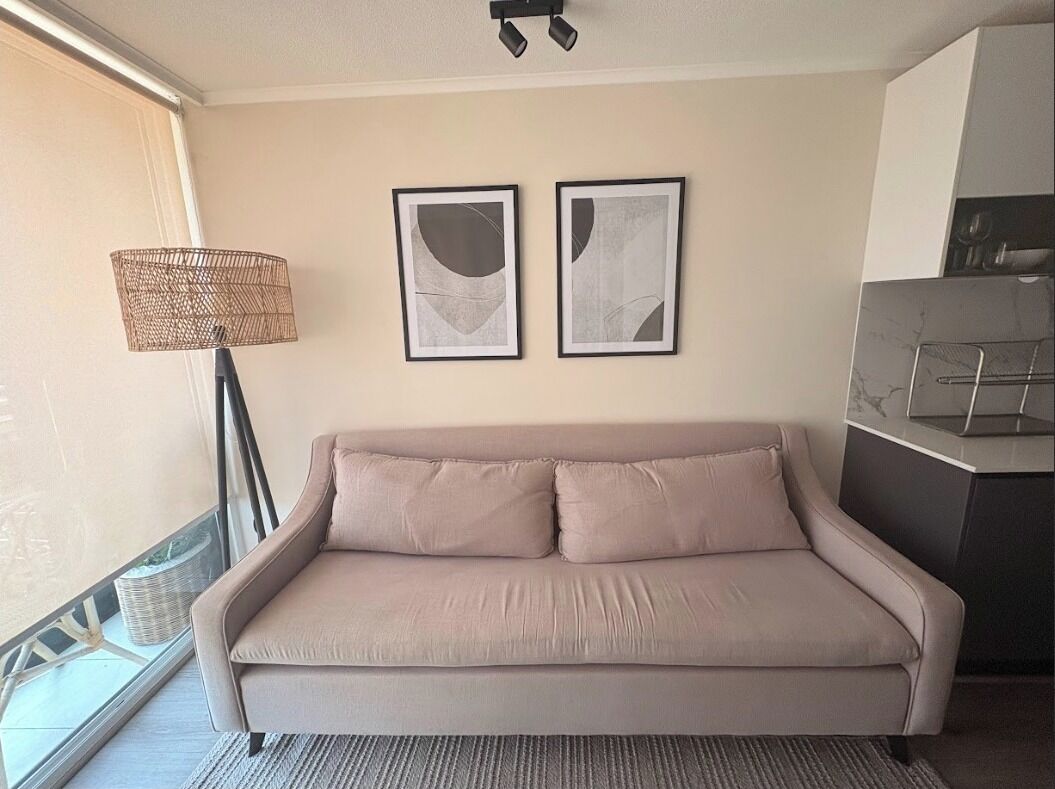 Ein sofa in neutralen Farbtönen in einem Raum mit einem großen Fenster, einer Stehlampe und zwei abstrakten Wandbildern.