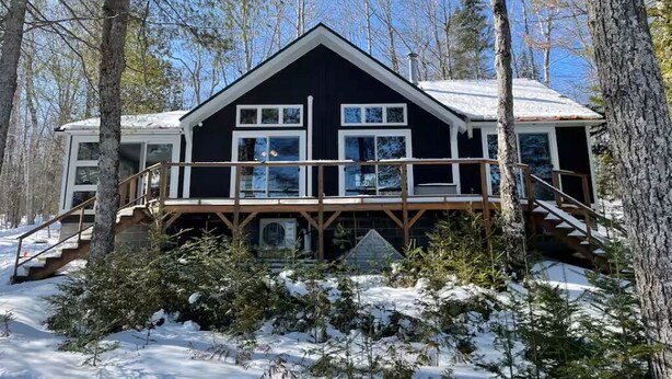 A cabin with a wooden deck, multiple windows, and a staircase leading to the entrance. - Amazing 4-bedroom cabin in Brownville perfect for your getaway (Brownville)