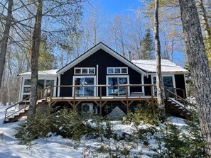 A cabin with a wooden deck, multiple windows, and a staircase leading to the entrance. - Amazing 4-bedroom cabin in Brownville perfect for your getaway (Brownville)
