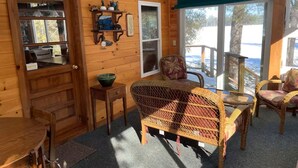 A wooden interior with a dining table, wicker chairs, a window with a view, and a door. - Amazing 4-bedroom cabin in Brownville perfect for your getaway (Brownville)