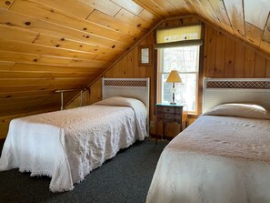 A room with two beds, wooden walls, a window with a lamp, and a small table. - Amazing 4-bedroom cabin in Brownville perfect for your getaway (Brownville)