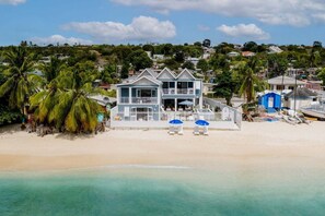 A beachfront property with a two-story house, a balcony, and a beach area with lounge chairs and umbrellas. - Beachfront Villa with Plunge Pool - Sea Breeze Beach Villa (Fitts Village)