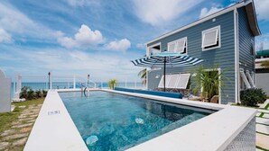 A swimming pool with a white deck, a blue house with shutters, and a clear sky. - Beachfront Villa with Plunge Pool - Sea Breeze House (4 bed) (Fitts Village)
