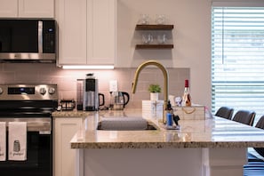 A modern kitchen with stainless steel appliances, a granite countertop, a gold faucet, and a dining area with a long table.