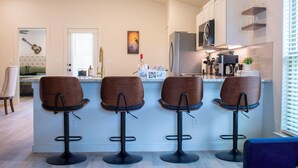 A modern kitchen with a bar area, featuring bar stools, a refrigerator, and a coffee machine. - New 3-bedroom, 2 bath, 2 car garage, home in exceptional south Lubbock location. (Lubbock)