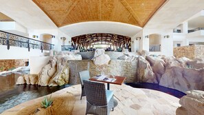 A spacious indoor area with a high ceiling, stone walls, and a central seating area with a table and chairs. - Two Bedroom Penthouse - Grand Solmar Lands End (Cabo San Lucas)