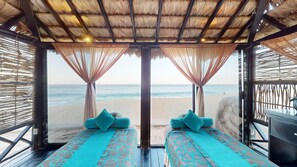 A beachside room with a thatched roof, two beds with patterned bedding, and a view of the beach. - Two Bedroom Penthouse - Grand Solmar Lands End (Cabo San Lucas)