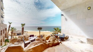 A beachside patio with stone seating, a table set for dining, and a view of the ocean. - Two Bedroom Penthouse - Grand Solmar Lands End (Cabo San Lucas)