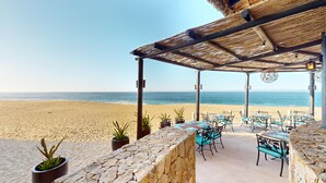 A beachside restaurant with outdoor seating, a stone wall, and a view of the ocean. - Two Bedroom Penthouse - Grand Solmar Lands End (Cabo San Lucas)