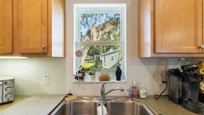 A kitchen with wooden cabinets, a stainless steel sink, a toaster, and a window with a view of a house and trees. -  Sublime Sunrise lakefront Dock, FirePit Kayak fishing Boat&boat trailer Parking (Hernando)