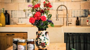 Uma cozinha com um vaso de flores, dois potes de compota e uma parede de tijolos rústicos.