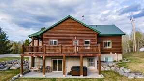 A two-story log cabin with a balcony, a covered porch, and a stone foundation.