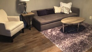 Un salon avec un canapé, un fauteuil, une petite table, une lampe et un tapis violet.