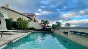 Une piscine à l’eau claire, entourée d’un petit muret et bordée d’un bâtiment dont le toit est recouvert de tuiles.