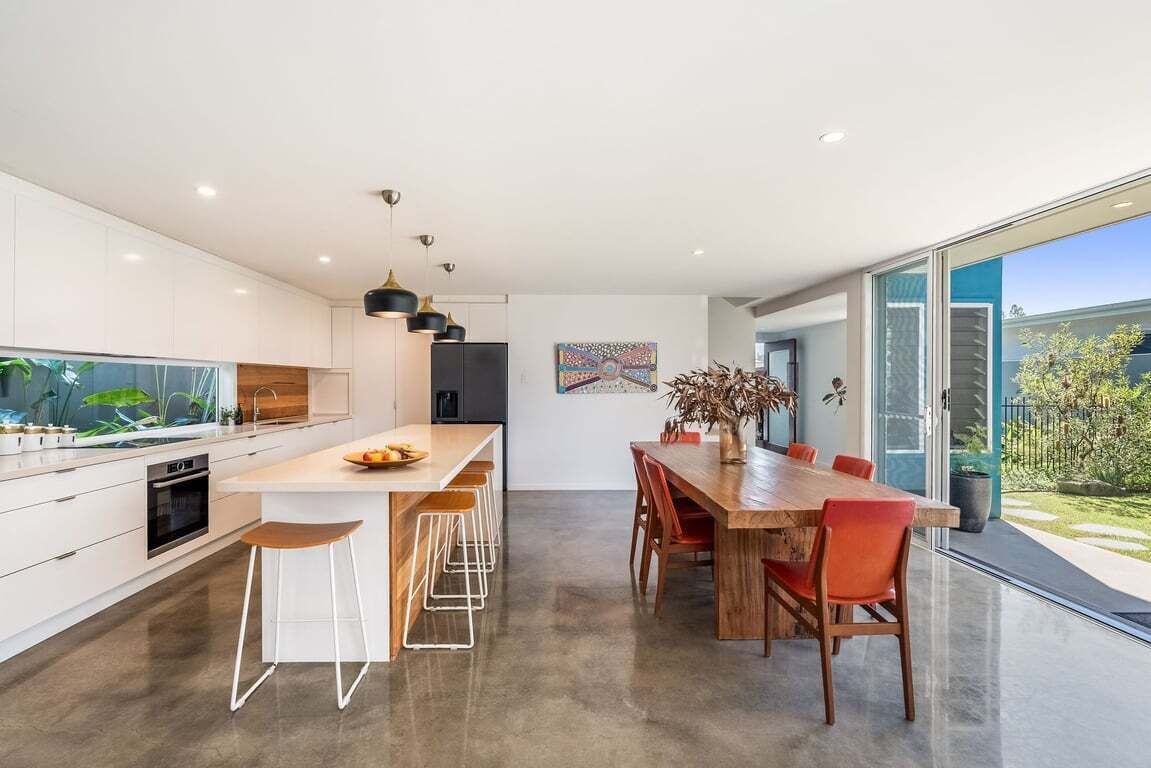 A modern kitchen with a central island, bar stools, and a dining table with chairs.