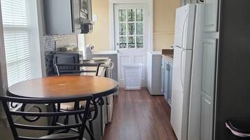 Una cocina con una mesa de comedor, sillas, un refrigerador y una ventana.