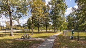 Un parc amb una taula de picnic, un camí per passejar i una zona tancada per una tanca.