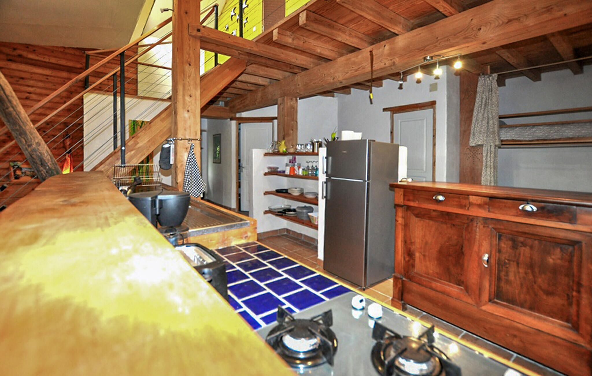 A kitchen with wooden beams, a gas stove, a refrigerator, and shelves with dishes.