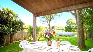 Een buiten eethoek met een ronde tafel voor vier personen, omringd door stoelen, onder een houten pergola.