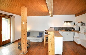 A compact kitchen with a wooden ceiling, a grey sofa, and a small dining area. - Authentique à la campagne (Cazalrenoux)
