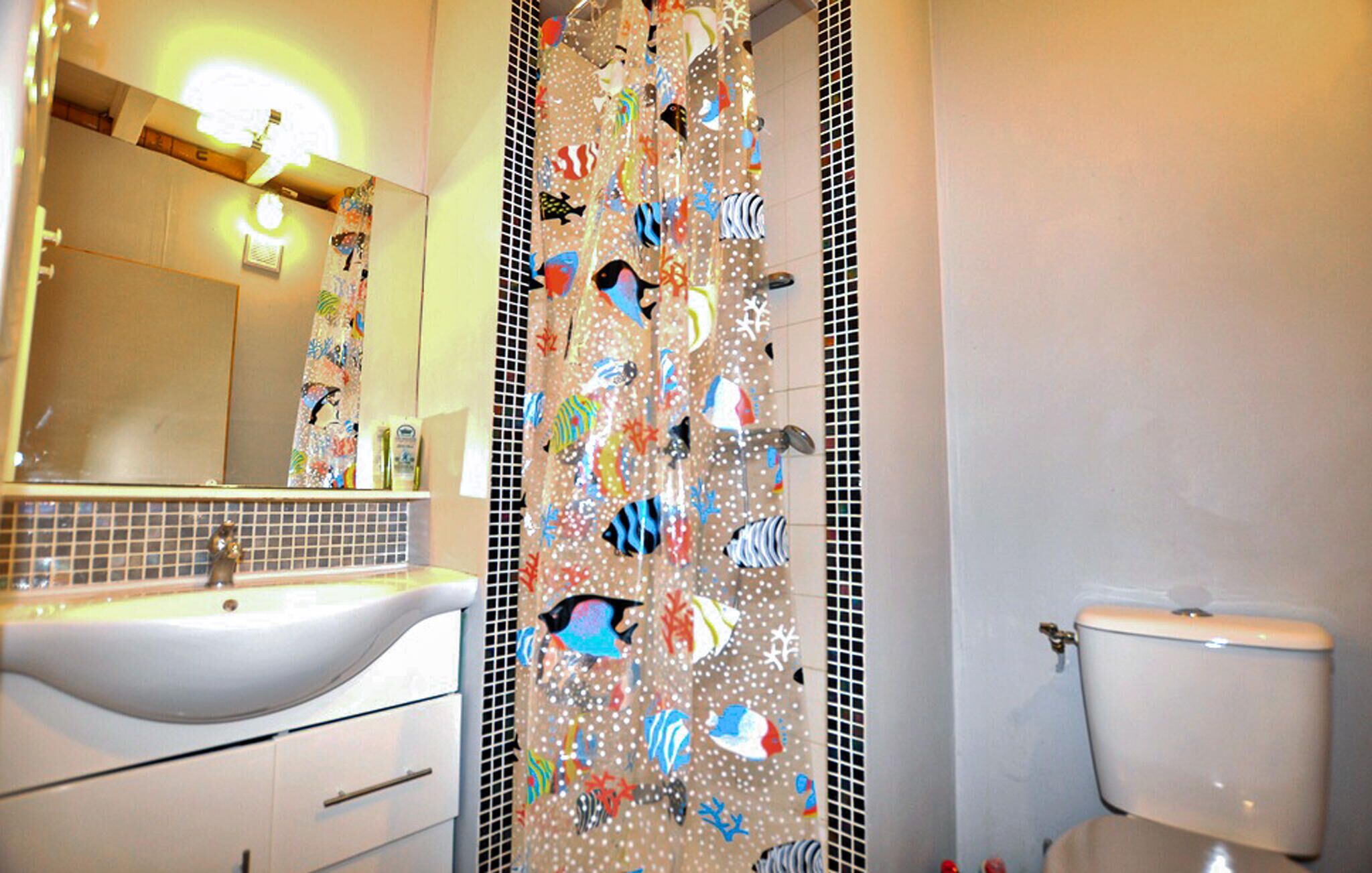 A bathroom with a white sink, a mirror, a shower curtain with fish patterns, and a toilet.