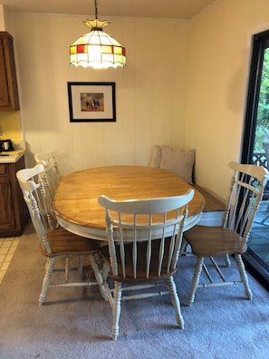 Un coin repas avec une table ronde en bois entourée de quatre chaises, un luminaire suspendu en vitrail et un tableau encadré au mur.