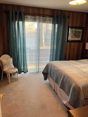 Une chambre à coucher avec un lit, une chaise, une fenêtre avec des rideaux et un tableau encadré au mur.