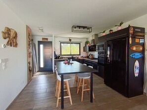 A modern kitchen with a central island, black appliances, and wooden stools. - Family house with private heated pool, air conditioning, pool view (Biscarrosse)