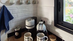 Une cuisine équipée d’une machine à café, de deux tasses, d’une horloge et d’un tableau encadré accroché au mur.