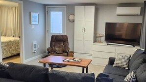 A compact living space with a sofa, a wooden table, a leather chair, a television, and a wardrobe.