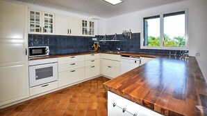 Une cuisine avec des meubles blancs, un four à micro-ondes, une cuisinière, un évier et une fenêtre donnant sur un paysage verdoyant.