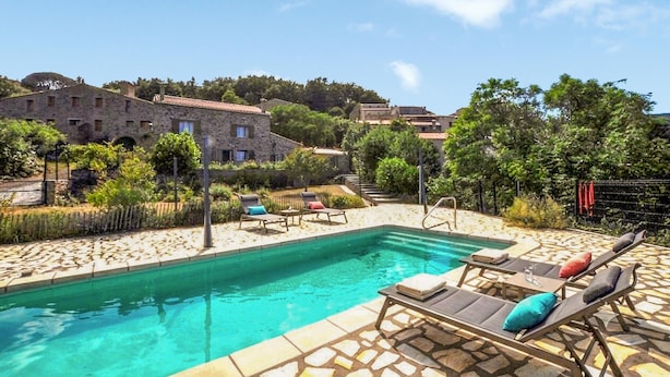 Un espace piscine avec des chaises longues et, en arrière-plan, un bâtiment en pierre.
