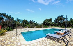 Ein rechteckiger Pool mit Steinrand, umgeben von Liegestühlen und einer Holzterrasse.