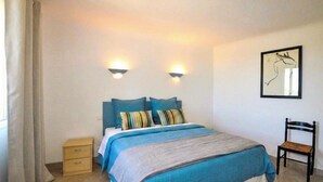 A bedroom with a bed, two bedside lamps, a chair, a nightstand, and a framed artwork on the wall. - Charmante villa piscine (Taulis)