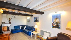 A room with a blue sofa, a small table, a chair, and a ship painting on the wall. - Charmante villa piscine (Taulis)