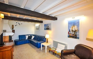 A room with a blue sofa, a small table, a chair, and a ship painting on the wall. - Charmante villa piscine (Taulis)