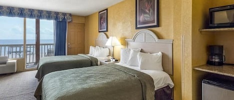 A hotel room with two beds, a desk, a chair, a television, and a view of the ocean.