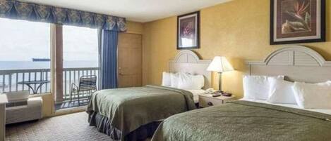 A hotel room with two beds, a balcony, and a view of the sea.