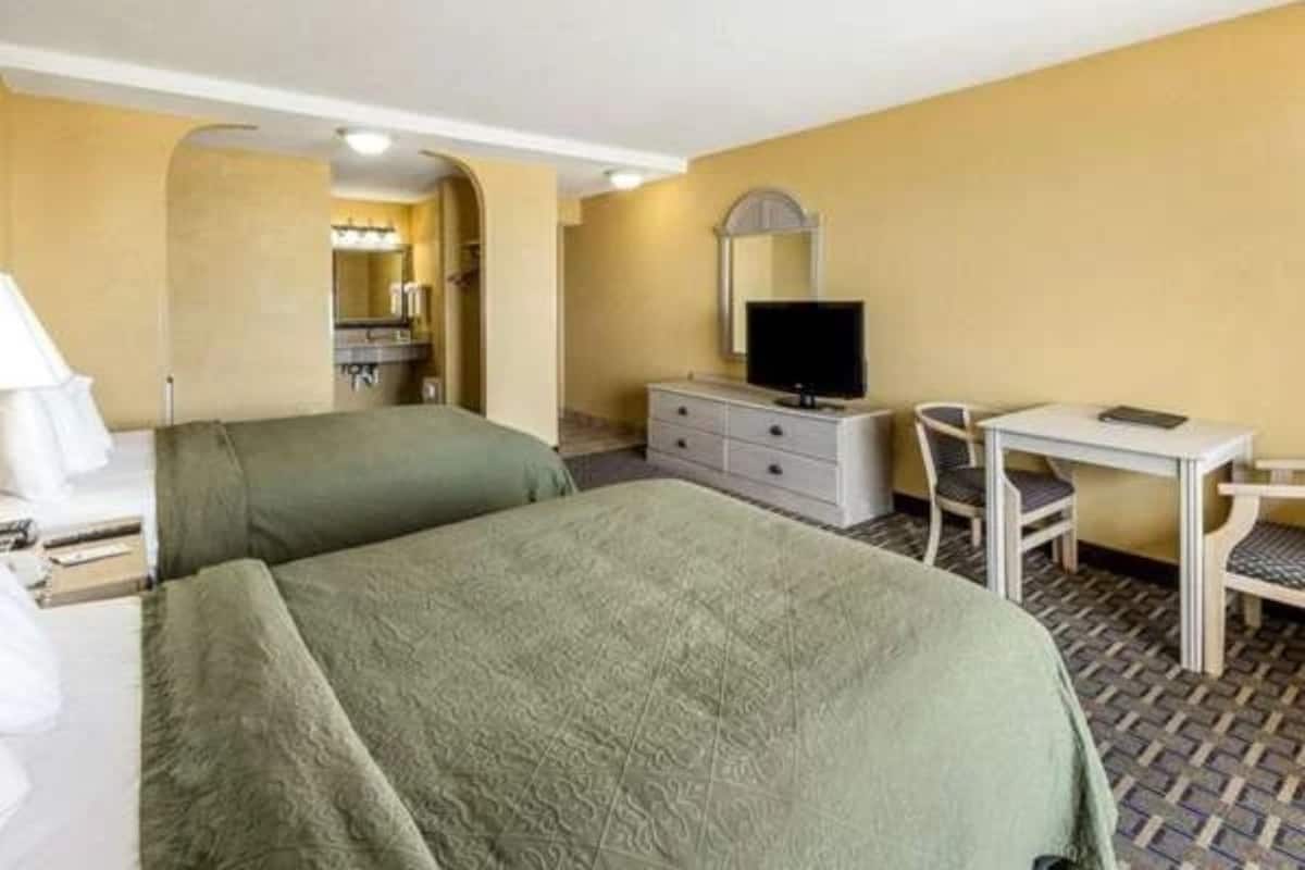 Ett hotellrum med två sängar, ett skrivbord, en stol, en tv och ett badrum som syns genom en valvöppning.