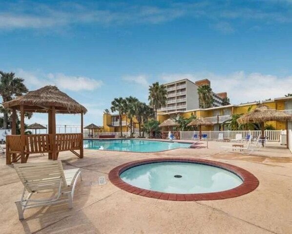 Une piscine avec un jacuzzi, des chaises longues et un pavillon à toit de chaume.