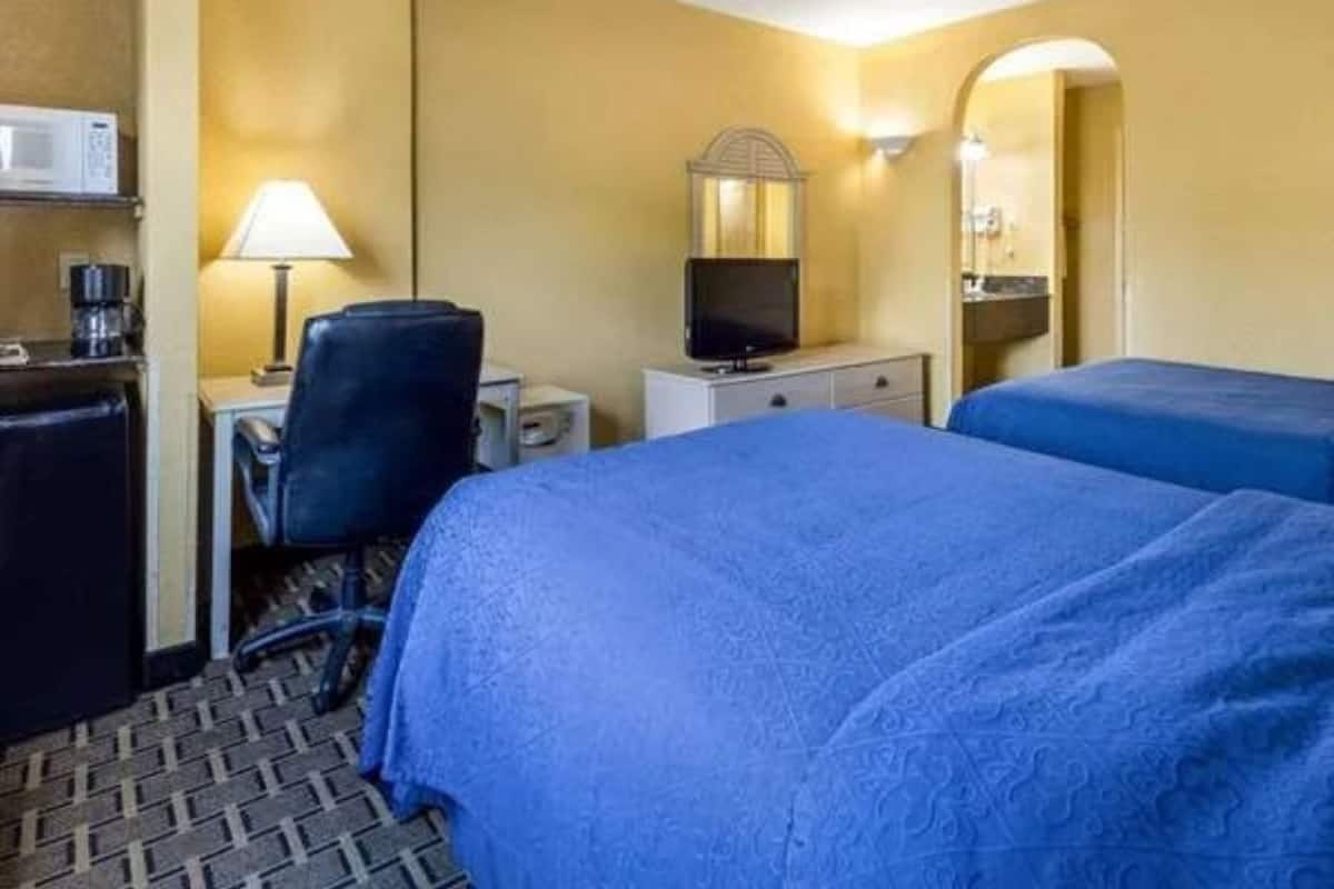 Ett hotellrum med två sängar, ett skrivbord med en lampa, en tv och en mikrovågsugn.