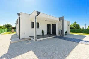 Un bâtiment moderne doté d’une entrée couverte, d’une allée en gravier et d’un petit jardin.