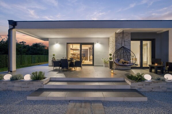 Una casa moderna amb un porxo cobert, seients exteriors i una cadira penjant.
