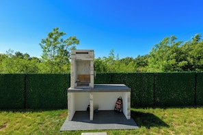 Ein Grill mit Schornstein, umgeben von einer Hecke und Rasen.