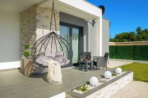Un espace extérieur moderne aménagé avec des sièges, comprenant un fauteuil suspendu, une petite table et une chaise.