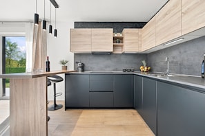 Eine moderne Küche mit dunklen Schränken, einer Holz Arbeitsplatte, einer Kaffeemaschine und Blick ins Freie.