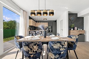 A modern dining area with a wooden table, chairs with a tropical leaf pattern, and a kitchen in the background. - Villa Maki (Istria - Svetvinčenat) (Svetvinčenat)